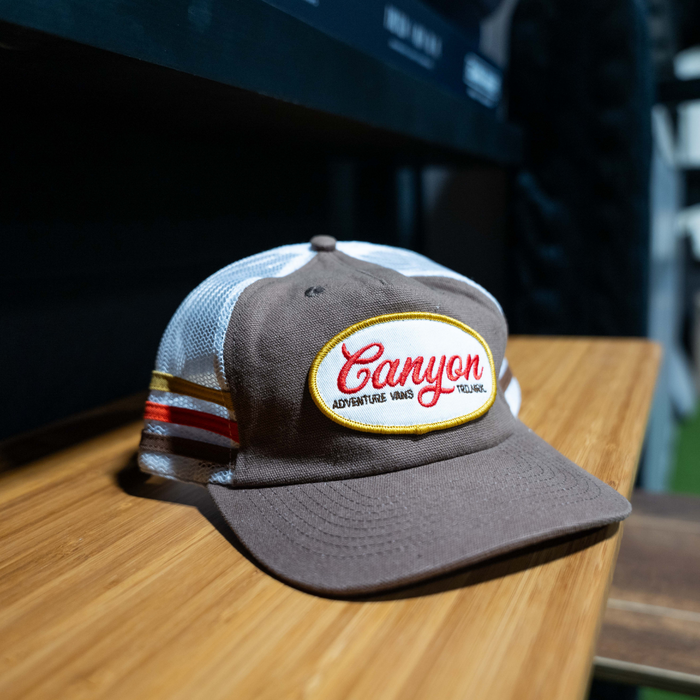 Brown and white Canyon CA Trucker Hat with mesh back and embroidered patch on wooden shelf