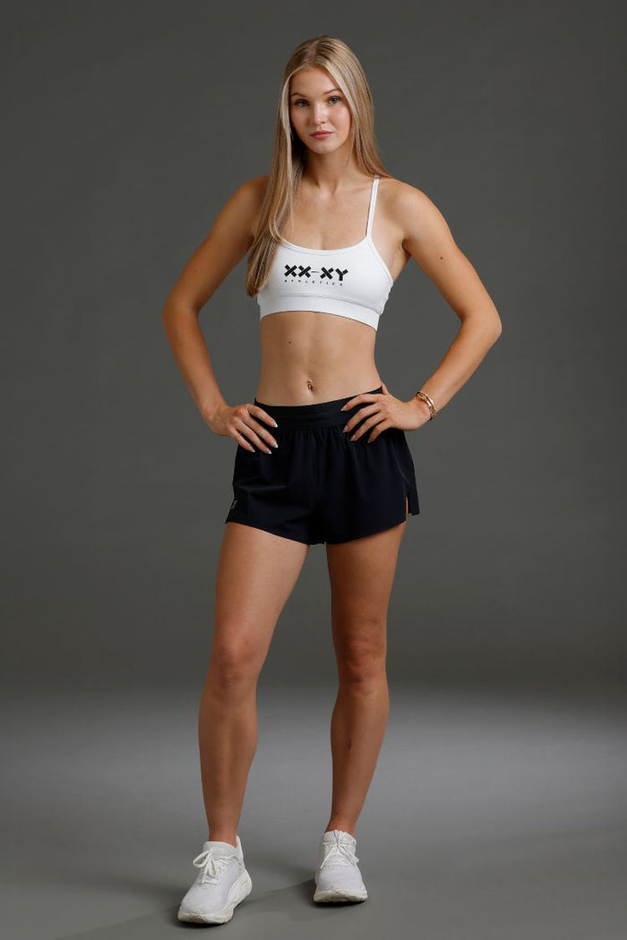 Woman wearing a white sports bra and black shorts on a gray background || Black