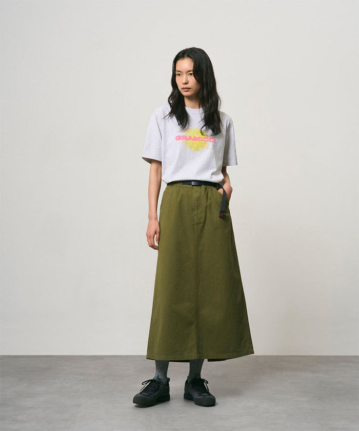 Model wearing a olive colored Gramicci 5-Pocket Skirt and a white shirt on a light-tone background.