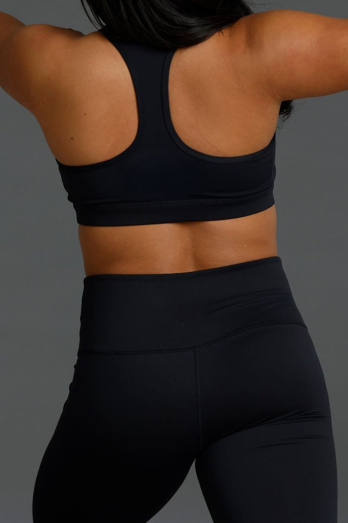 Person wearing a black sports bra and leggings on a gray background || Black