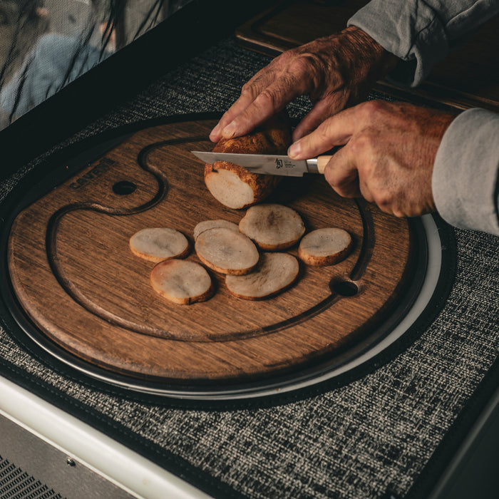 Person slicing root vegetables on a round bamboo sink cover in a van kitchen