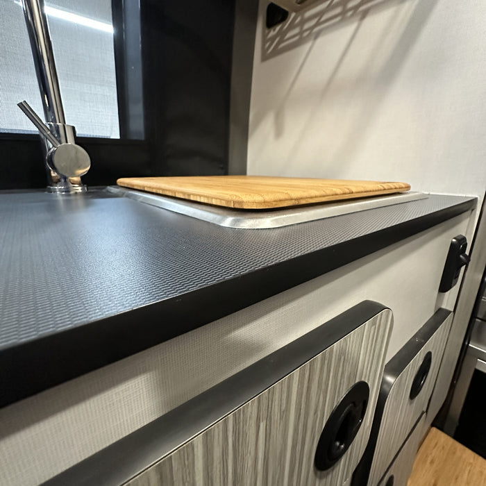 Bamboo sink cover on van kitchen counter with faucet and cabinetry visible