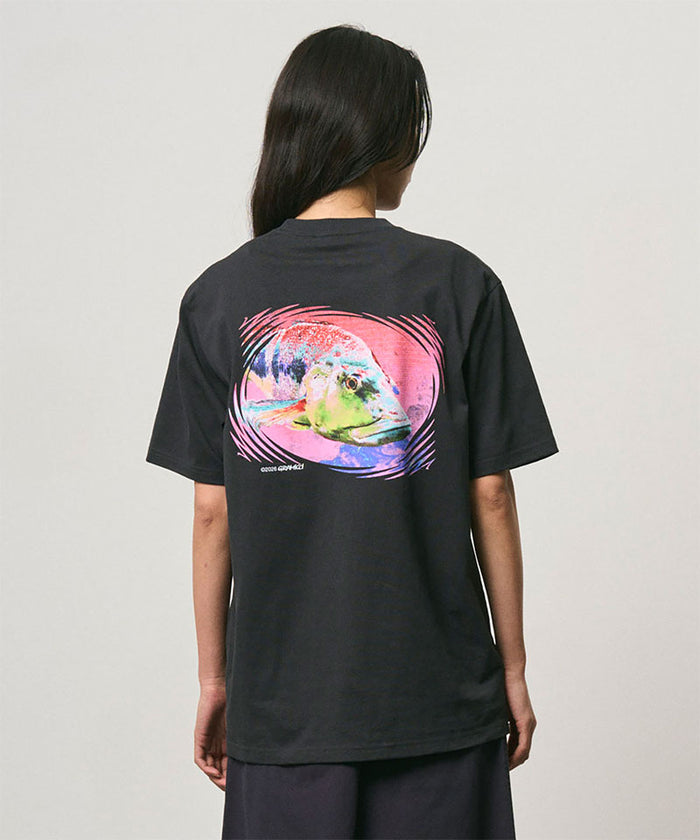 Back view of a model wearing a Gramicci vintage black Bass Tee with a graphic against a light-tone background.
