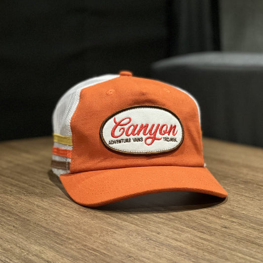 Orange and white Canyon Adventure Vans trucker hat on a wooden surface