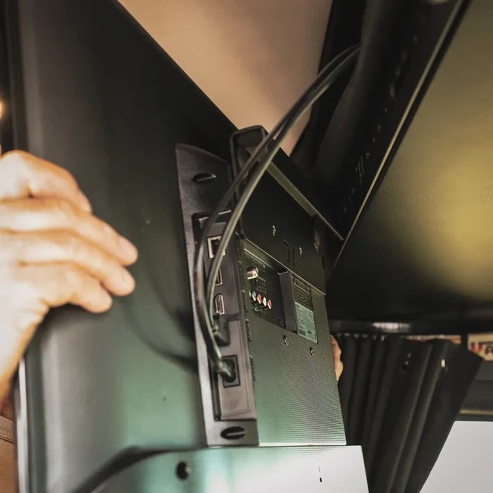 Person installing a Cab Shelf TV Bracket inside a van with a mounted flat-screen TV.