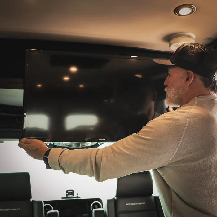 Man installs Cab Shelf TV Bracket in a van interior under overhead cabinet lighting.