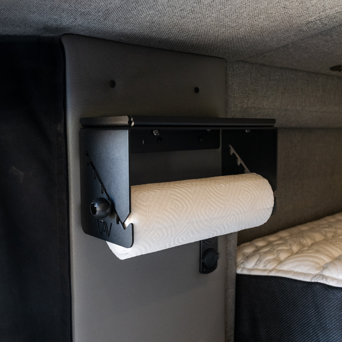 Canyon paper towel holder mounted on a van wall above a bed with quilted bedding.