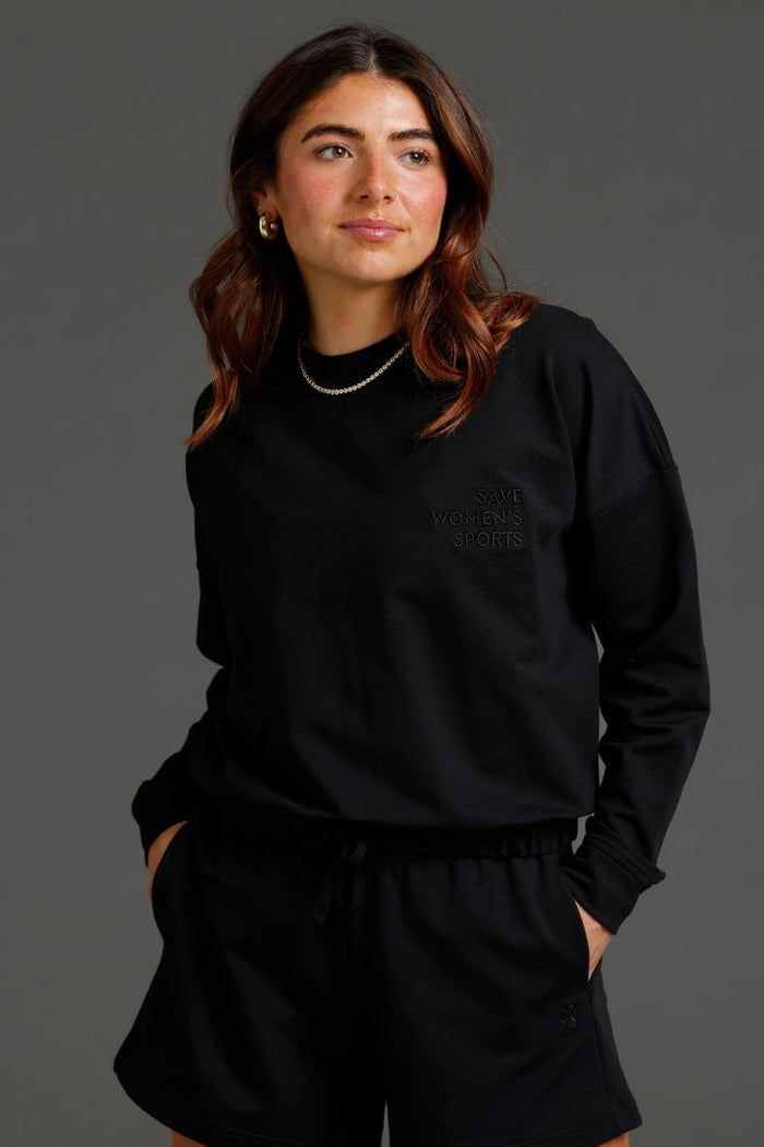 Person wearing a black outfit with a logo on a gray background || Black
