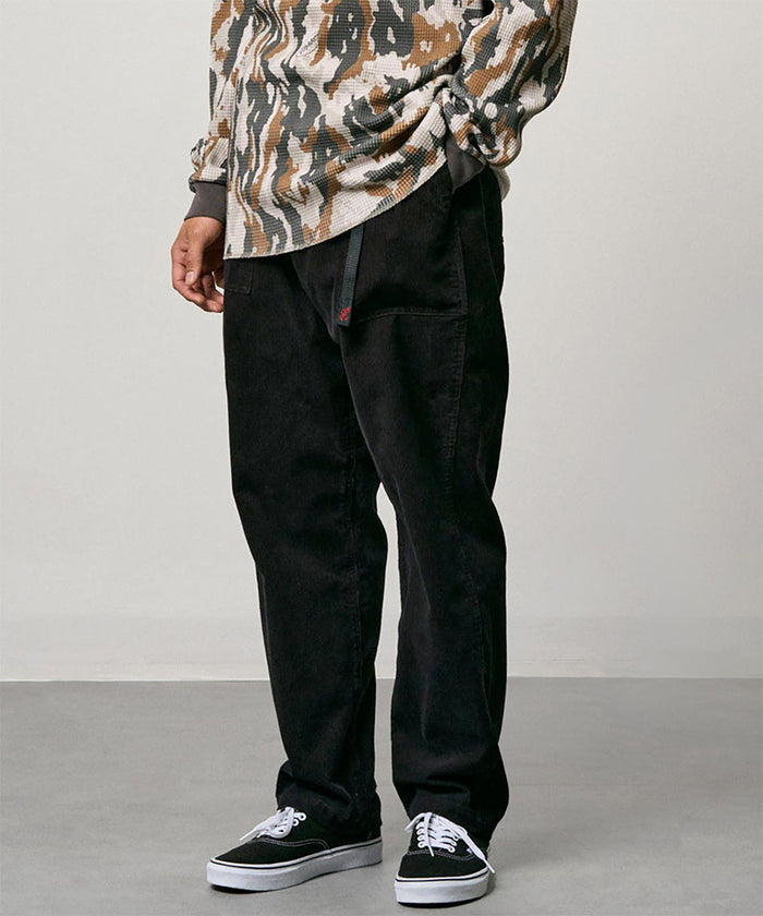 Model wearing black Gramicci Corduroy Loose Tapered Ridge Pants and a camo shirt on a light-tone background.