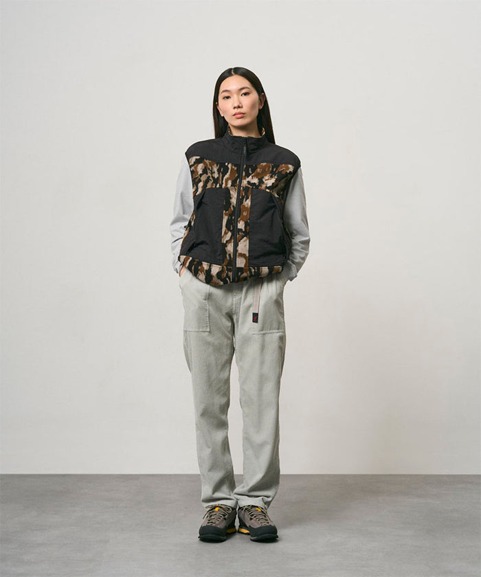 Model wearing smokey grey Gramicci Corduroy Loose Tapered Ridge Pants and a camo black jacket on a light-tone background.