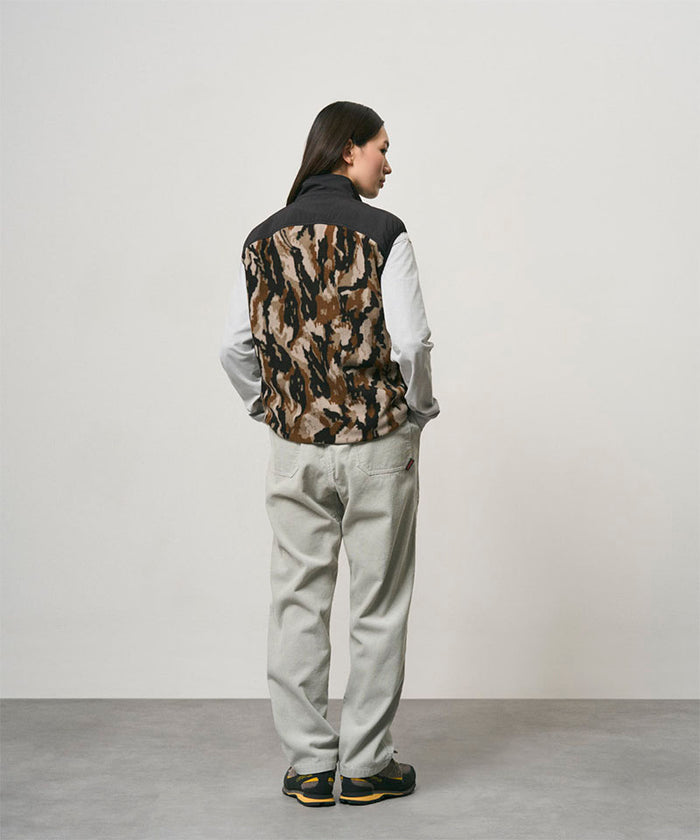 Back view of a model wearing smokey grey Gramicci Corduroy Loose Tapered Ridge Pants and a camo black jacket on a light-tone background.