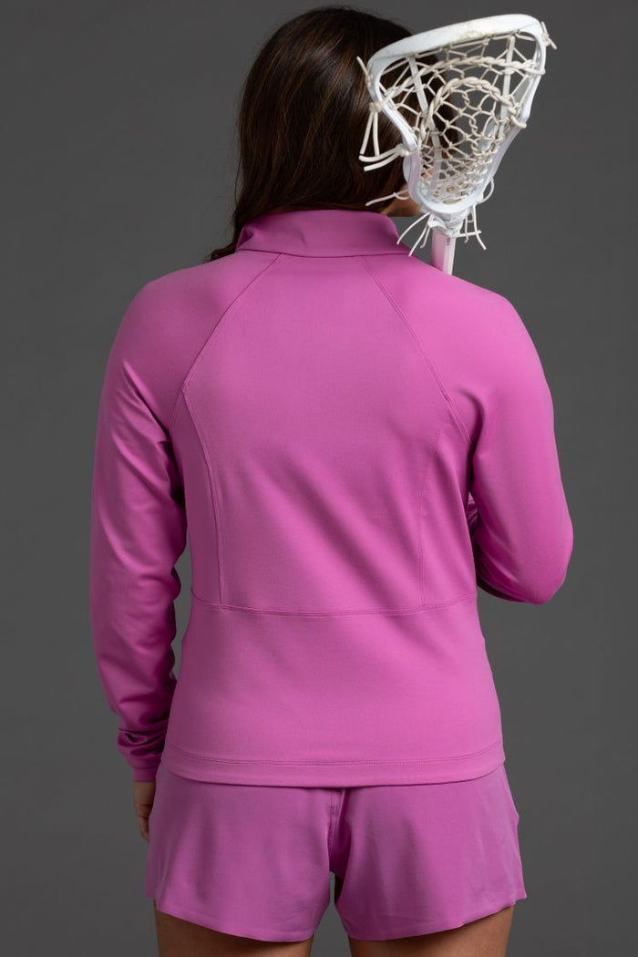 Person wearing a pink athletic outfit with a lacrosse head on a gray  background || Bright Fuchsia