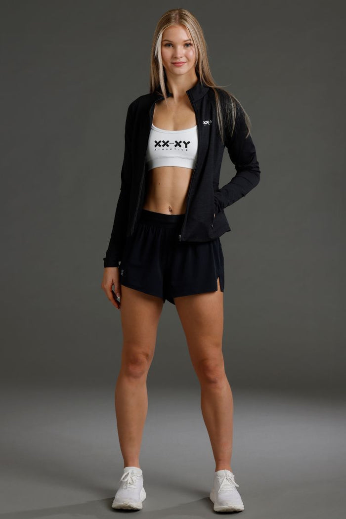 Woman wearing a black jacket, white sports bra with 'XY' logo, and black shorts || Black