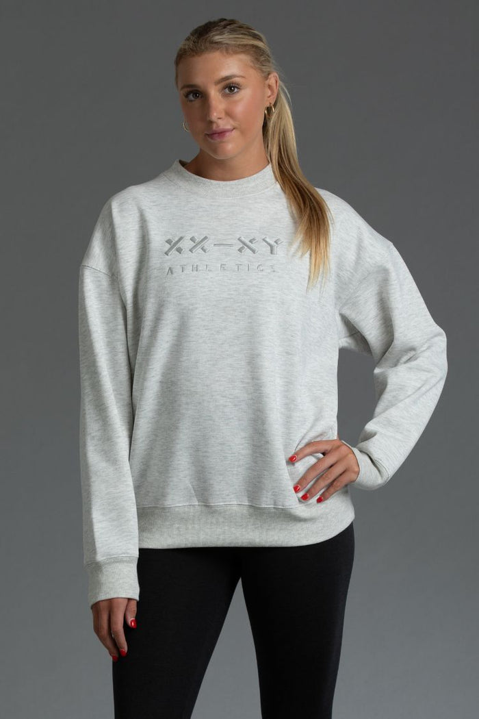 Woman wearing a gray sweatshirt with a logo on a gray background || Light Heather Gray