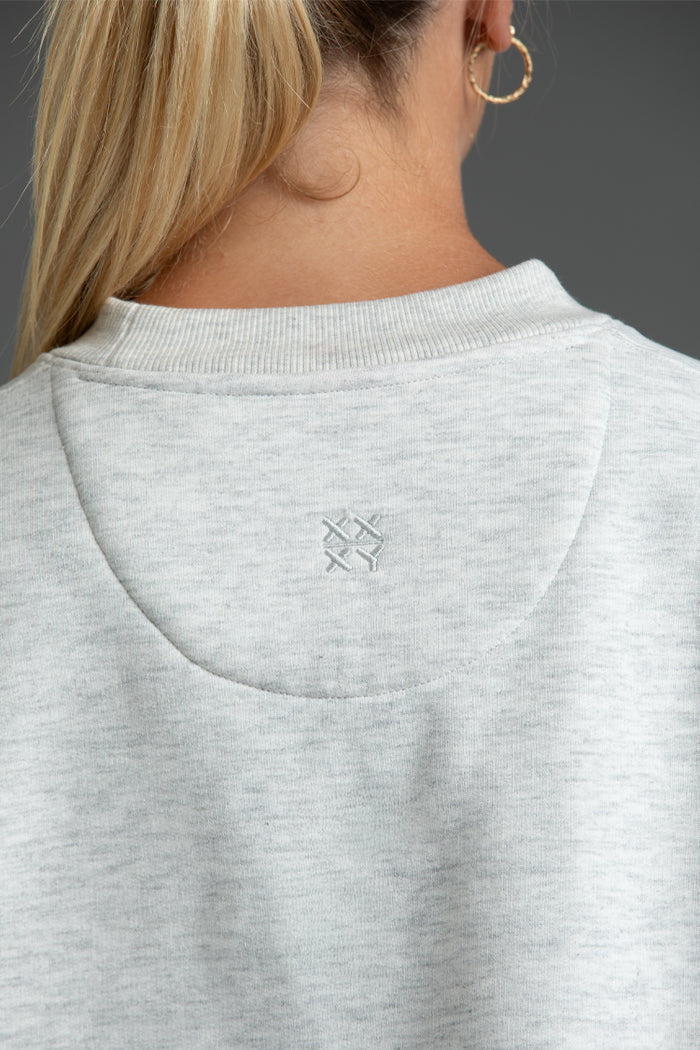 Gray sweatshirt with a small logo on the collar, worn by a person. || Light Heather Gray