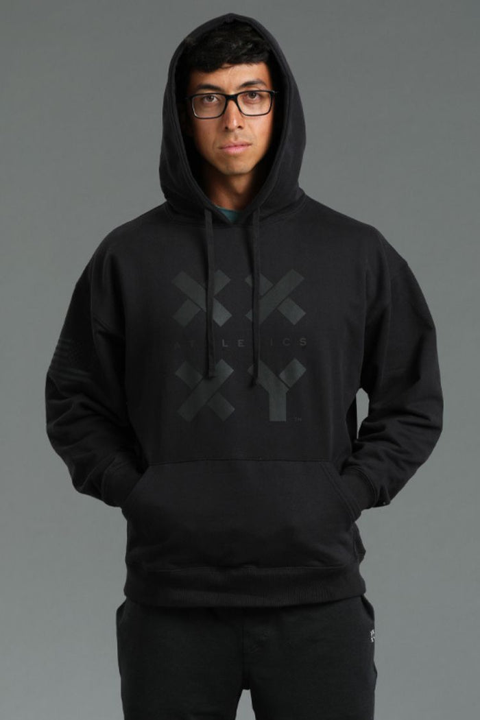 Person wearing a black hoodie with a logo on a gray background || Black