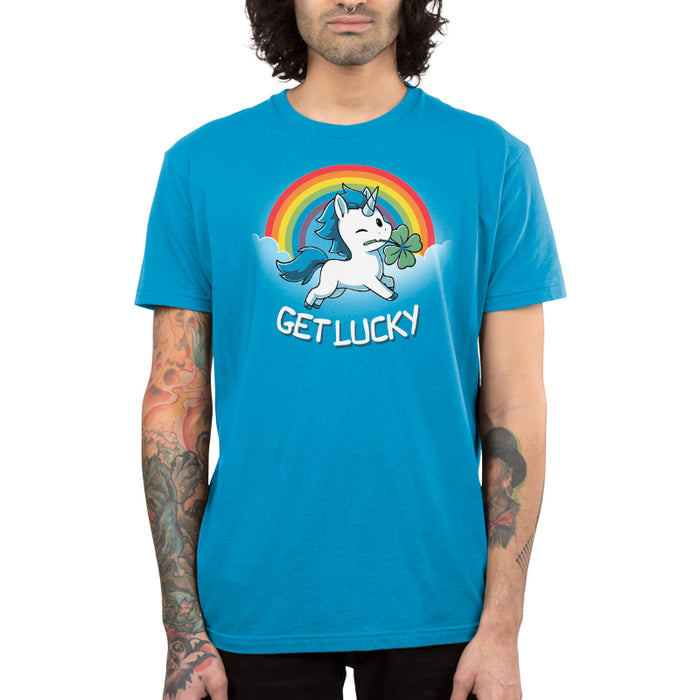 Premium Cotton T-shirt_Teeturtle cobalt blue Get Lucky apparel featuring a winking white unicorn holding a four-leaf clover while jumping through the clouds with a rainbow behind it. Caption reads, "get lucky".