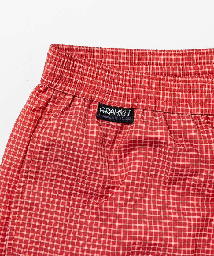 Front view close-up of red checkered Gramicci Grid Swim Shorts against a light-tone background.