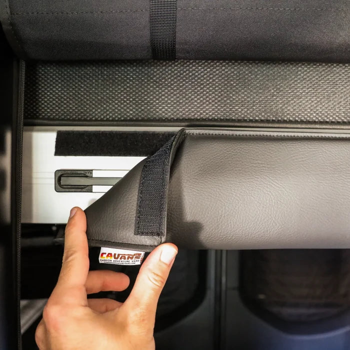 Hand lifting CAV cushion to reveal mounting rail inside a Revel van interior.