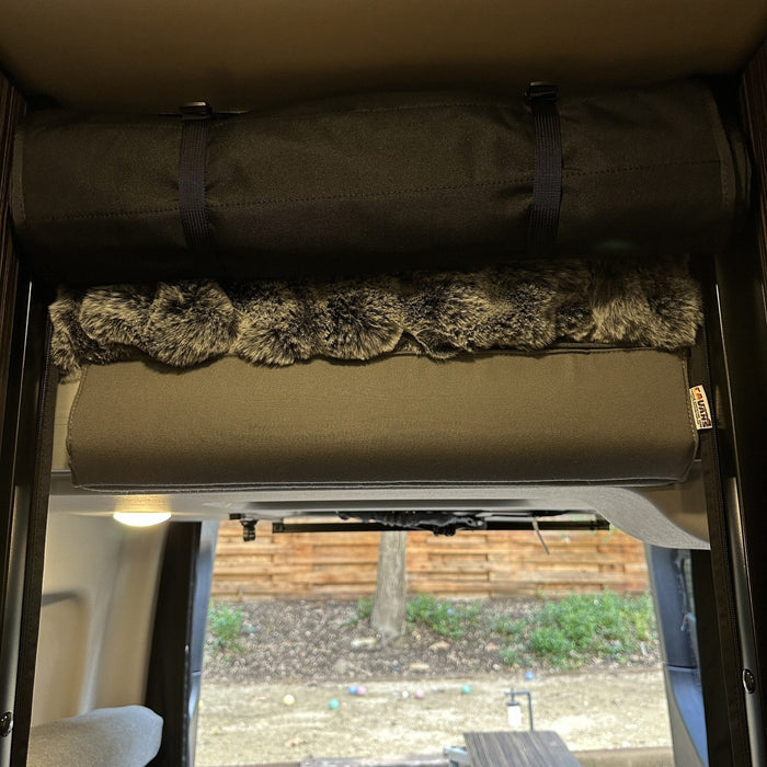 Head bumper with faux fur cover installed above bed in a 2019+ Revel van interior.
