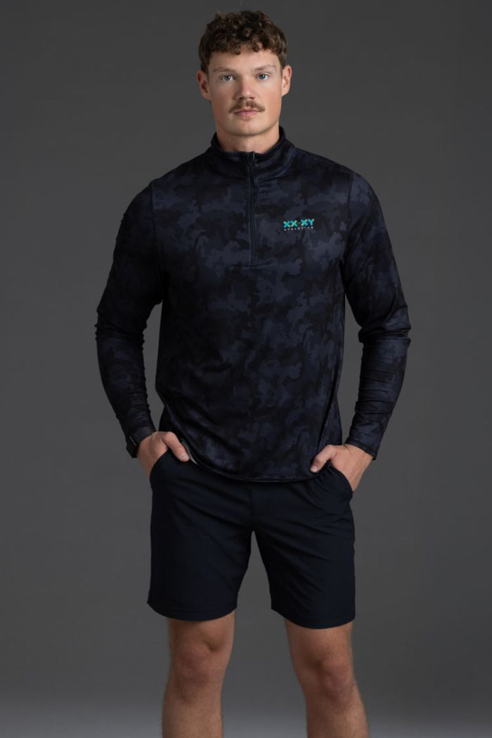 Man wearing a dark patterned long-sleeve shirt and black shorts on a gray background || Black Camo