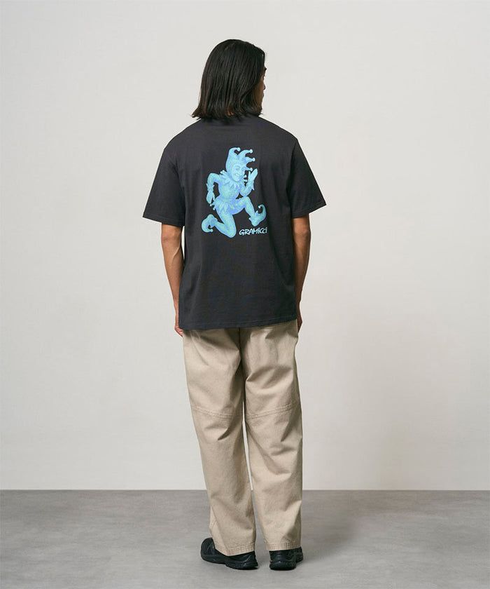 Back view of a model wearing a vintage black Gramicci Joker Tee with a teal graphic and beige pants on a light-tone background.