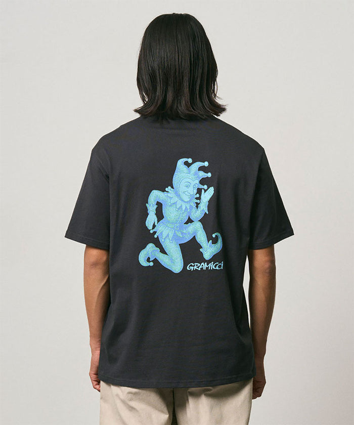 Back view of a model wearing a Gramicci vintage black Joker Tee with a teal graphic against a light-tone background.