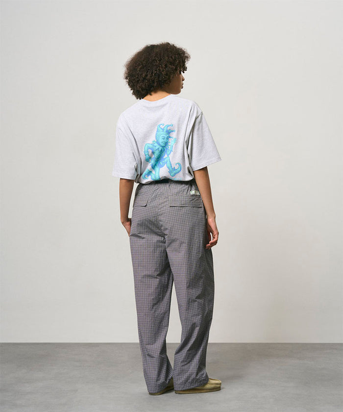 Back view of a model wearing a ash heather color Gramicci Joker Tee with a teal graphic and grey pants on a light-tone background.