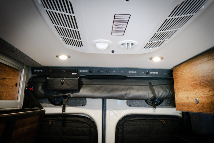 L-Track PRO mounted above rear doors inside a Storyteller Overland van with wood cabinets and gear storage.