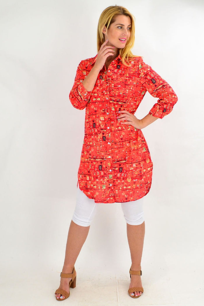 Long orange abstract tunic shirt by Ruby Rain with flowing fabric and vibrant print, displayed hanging on a plain background.