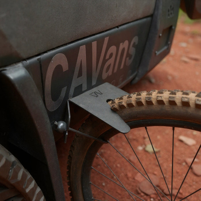 Rear wheel of a bike mounted on a CAVans magnetic bike stand near a van on a dirt trail