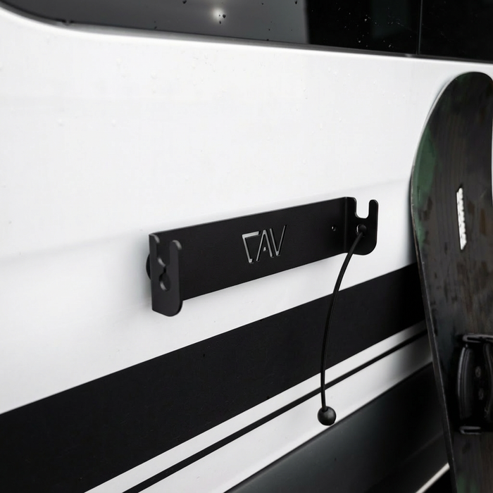 CAV magnetic ski and snowboard holder mounted on van exterior with a snowboard leaning nearby