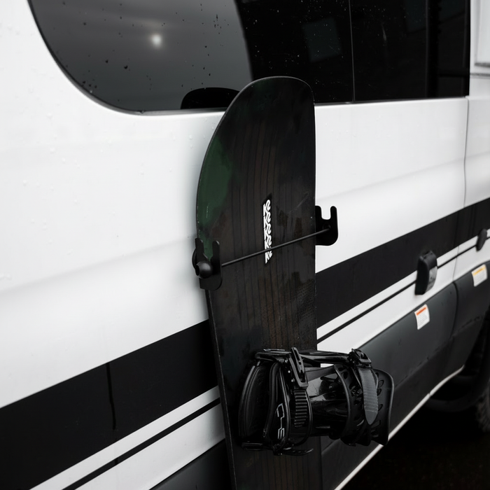 Revel magnetic snowboard holder mounted on the side of a van holding a black snowboard upright.