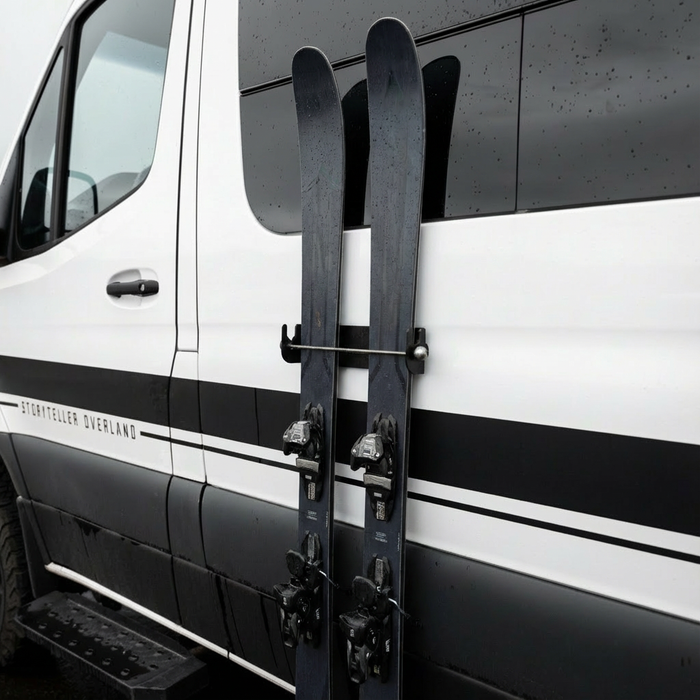 Magnetic ski holder mounted on the side of a Storyteller Overland van holding two skis upright.
