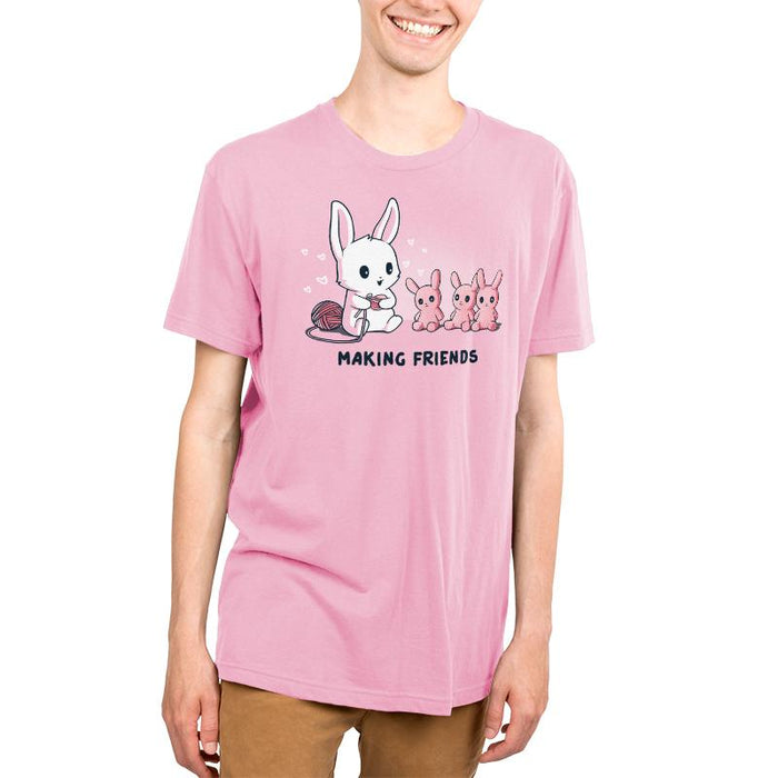 Premium Cotton T-shirt_Teeturtle light pink Making Friends apparel featuring a white bunny knitting 3 bunny friends out pink of yarn, caption reads, "Making Friends'.