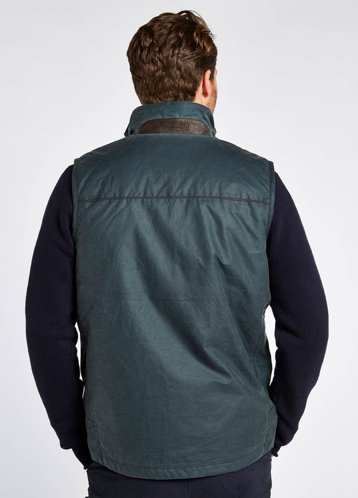"Waist up view of a male model showing the back of a Dubarry Mayfly Wax Jacket for men, dark pebble blue green coloured longer length jacket with a brown leather panel on back of collar. 
"