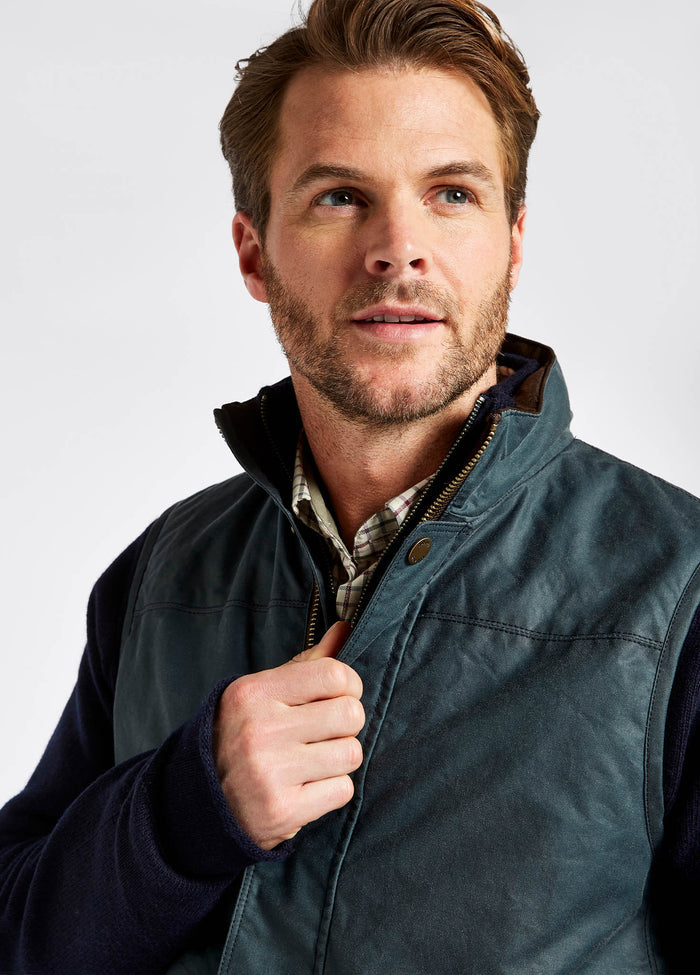 Close up of the collar on Dubarry Mayfly wax gilet jacket for men. Dark pebble green blue coloured gilet with inside collar of the jacket is a lighter shade of brown with buttons along the zip. Signature leather Dubarry label is stitched inside the jacket