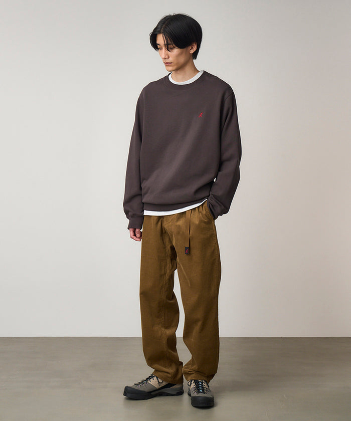 Model wearing a deep brown Gramicci One Point Crew Sweatshirt and brown pants on a light-tone background.