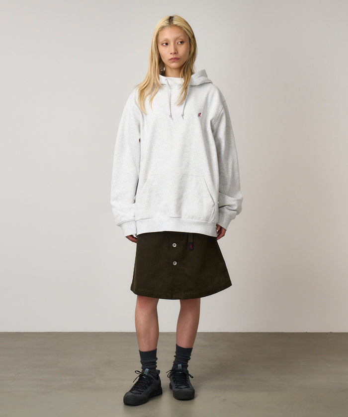 Model wearing a heather ash colored Gramicci One Point Hooded Sweatshirt and dark skirt on a light-tone background.