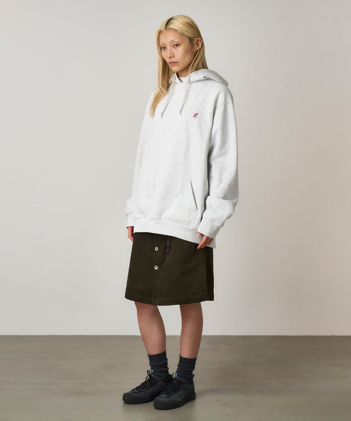 Model wearing a heather ash colored Gramicci One Point Hooded Sweatshirt and dark skirt on a light-tone background.
