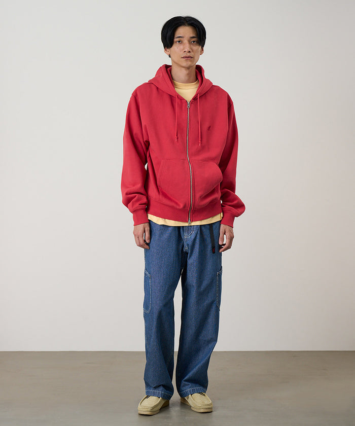 Model wearing a crimson red Gramicci One Point Zip Hooded Sweatshirt and blue pants on a light-tone background.