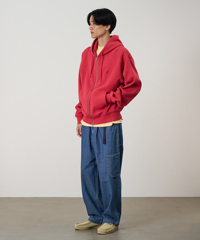 Model wearing a crimson red Gramicci One Point Zip Hooded Sweatshirt and blue pants on a light-tone background.