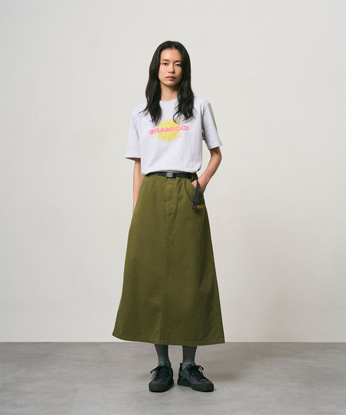 Model wearing a ash heather colored Gramicci Starburst Tee with a graphic and olive skirt on a light-tone background.