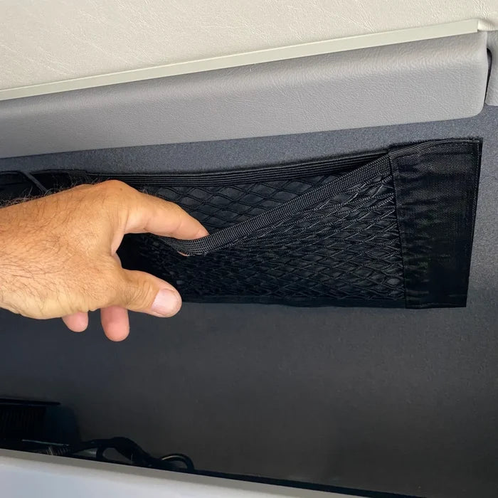 Hand opening a black mesh storage net mounted to a van wall.
