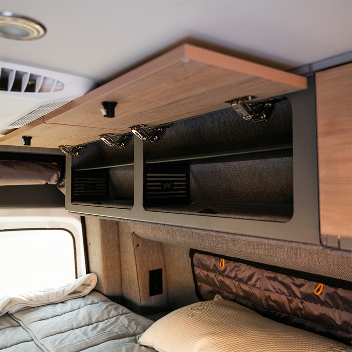 Open Storyteller overhead cabinet shelf in van interior with wood finish and black compartments.