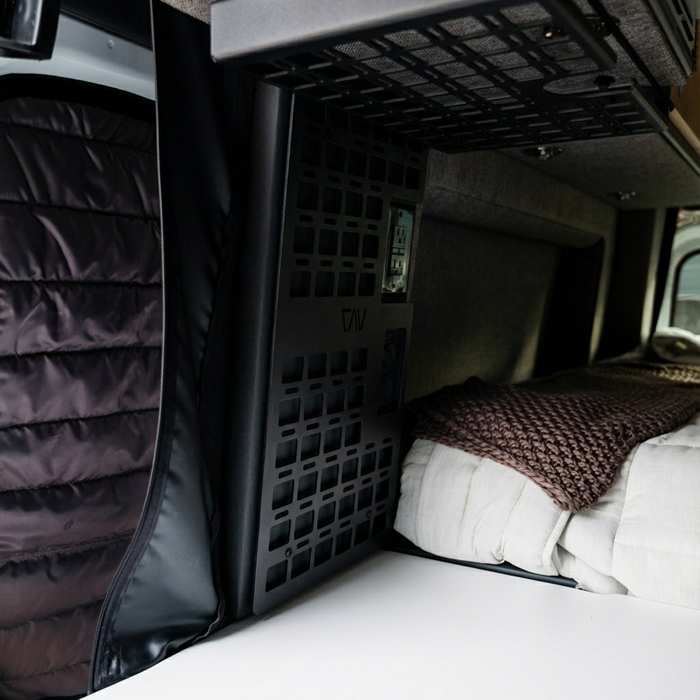 Storyteller MOLLE panel installed in van next to bed with brown quilt and gray padded wall.