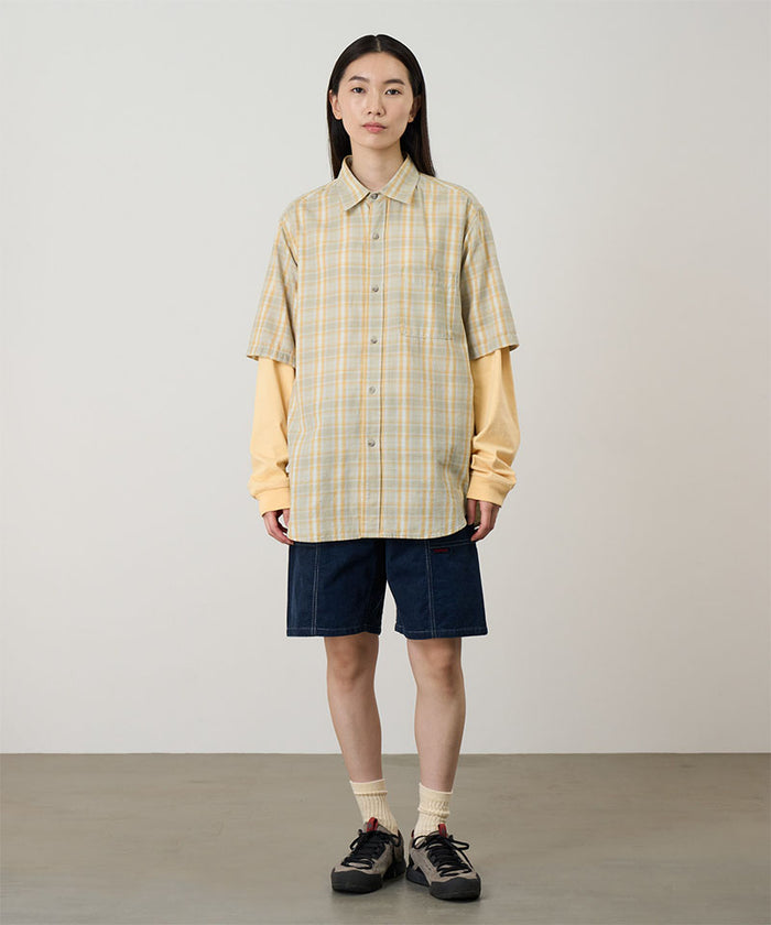 Model wearing beige Gramicci Women's Corduroy Utility Short and a green plaid shirt on a light-tone background.